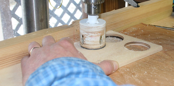 drill press with hole saw attachment cutting a circlular piece of plywood
