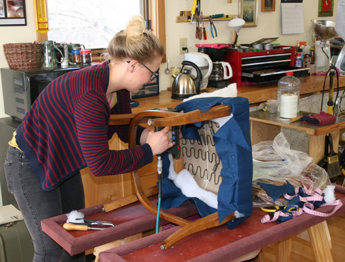 Upholstery student stapling seat fabric to her window back dining chair
